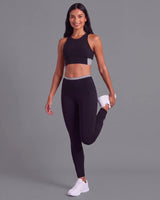 Smiling woman standing on one leg with the other knee bent behind her, wearing Black High-Rise Leggings and a matching sports bra.