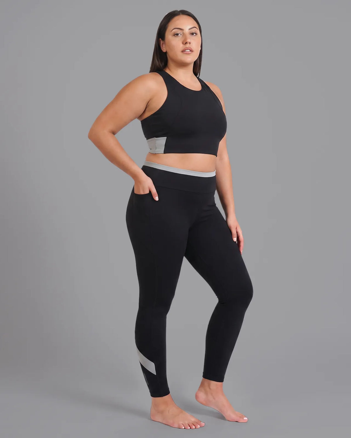 Three-quarter view of a model in the Black Full Coverage Sports Bra and High-Rise Leggings, one hand tucked into the side pocket.