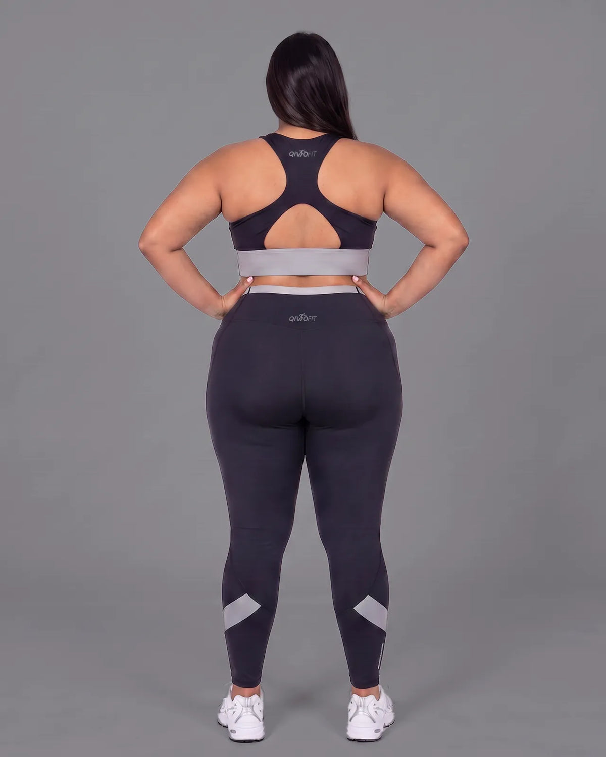 Full-length back view of the Black sports bra and leggings, hands on her hips, showing the racerback construction, keyhole opening and fit through the hips.