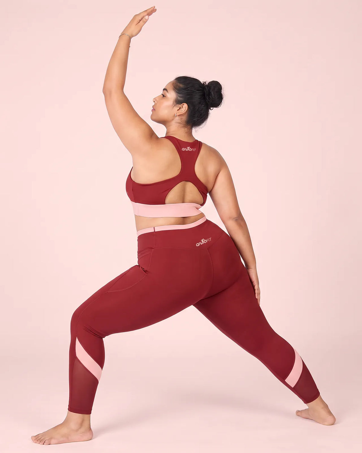 Back view of a woman in a wide warrior stance, one arm raised, wearing Maroon High-Rise Leggings and a matching racerback sports bra.
