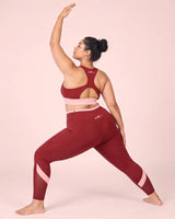 Back view of a woman in a wide warrior stance, one arm raised, wearing Maroon High-Rise Leggings and a matching racerback sports bra.