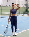 Woman on a tennis court holding a racket, wearing QivoFit Navy High-Rise Leggings with no front seam and light blue calf panels, with a matching sports bra.