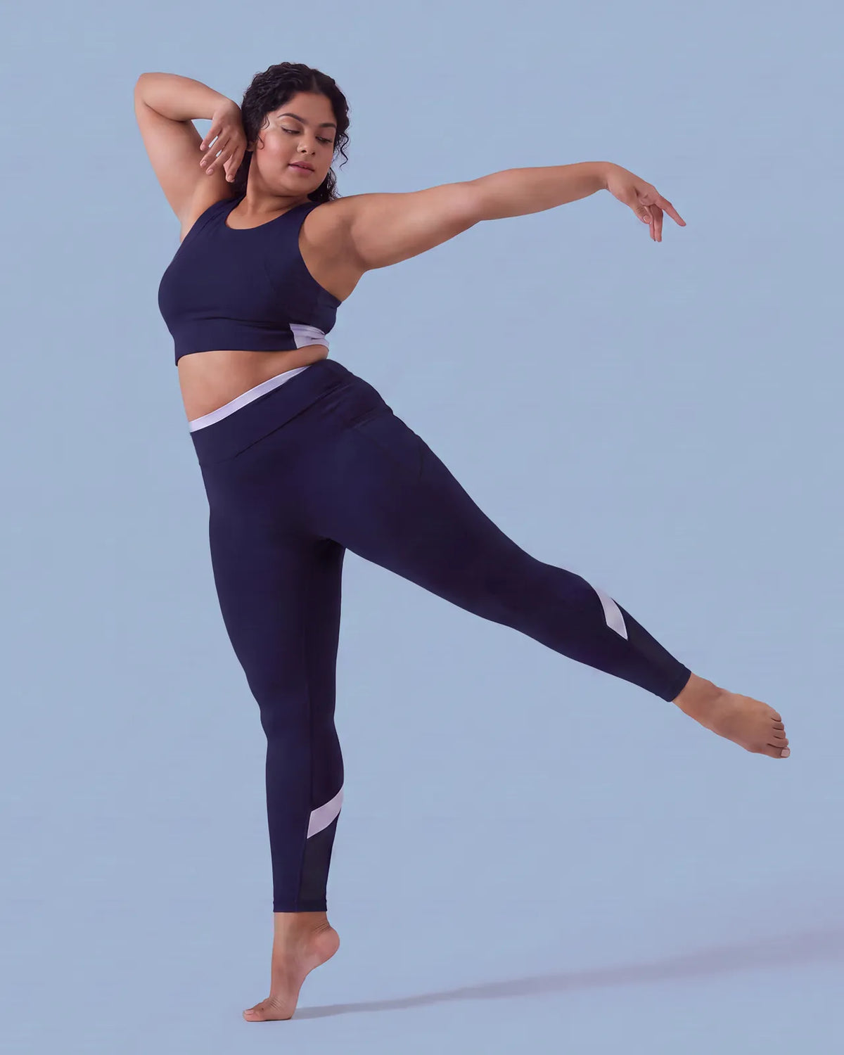 Woman mid-dance with one leg extended behind her and arms outstretched, wearing the Navy Full Coverage Sports Bra and High-Rise Leggings.