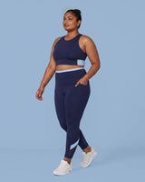 Woman walking in the Navy Full Coverage Sports Bra and High-Rise Leggings, one hand tucked into the side pocket.