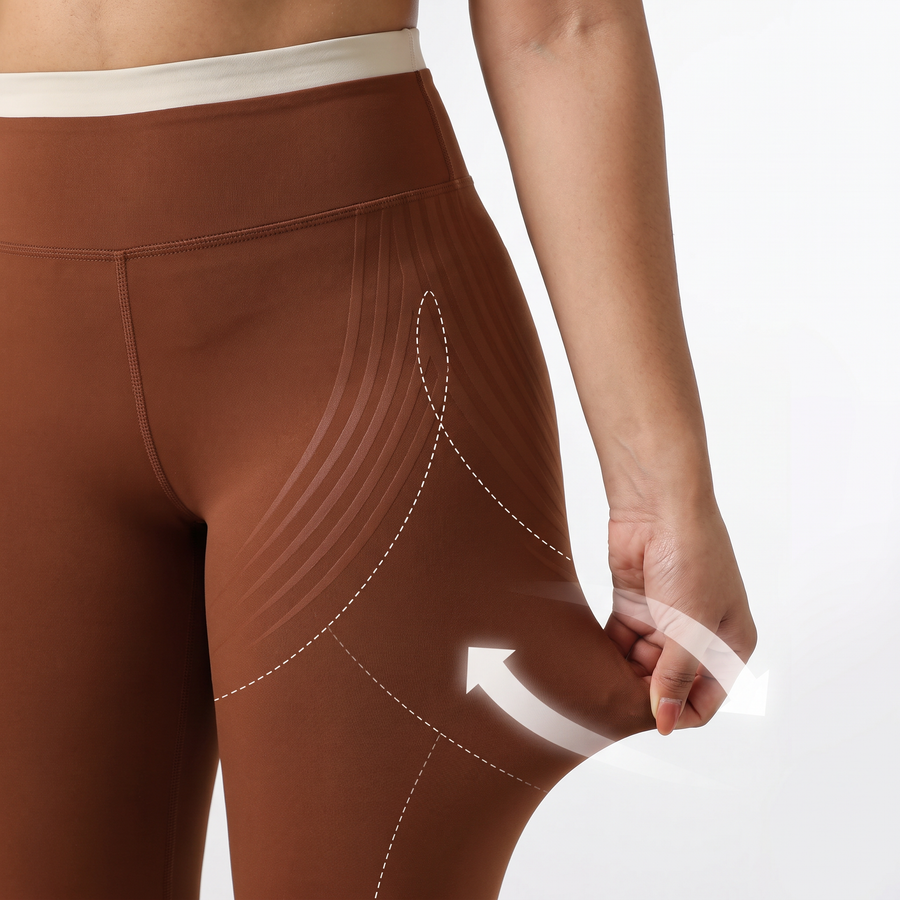 Hand pulling the fabric of brown leggings at the hip, with arrows showing the stretch in every direction.