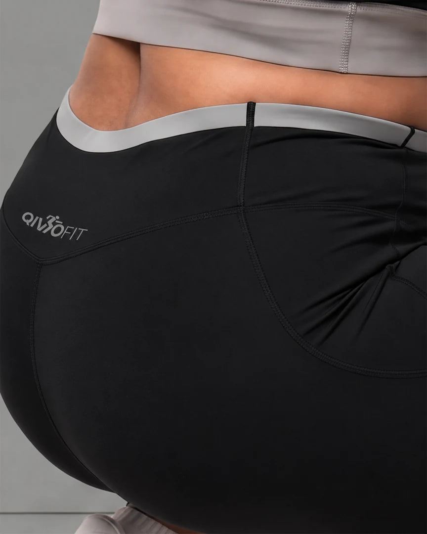 Close-up of the back of QivoFit’s black leggings: thick grey contrast waistband, QivoFit logo and contoured seams that follow the body.