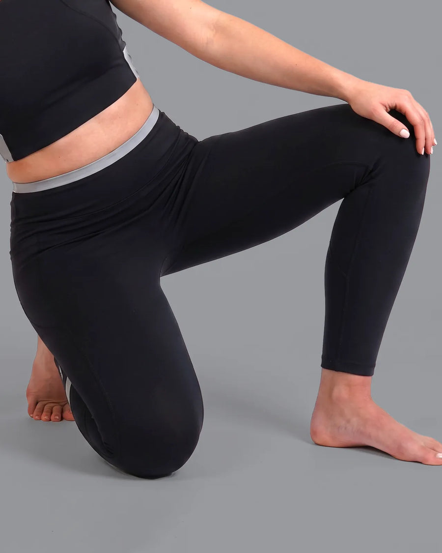Woman kneeling on one knee in Black High-Rise Leggings with a grey waistband, showing a clean fit through the gusset mid-lunge.