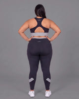 Full-length back view of the Black sports bra and leggings, hands on her hips, showing the racerback construction, keyhole opening and fit through the hips.