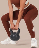 Woman in a deep squat holding a kettlebell, wearing Brown High-Rise Leggings, showing the waistband and fit holding through the movement.