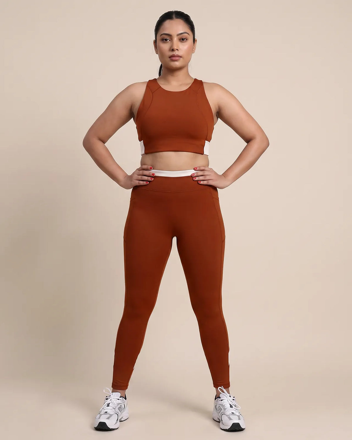 Full-length front view of a model in the Brown Full Coverage Sports Bra and High-Rise Leggings, hands on her hips.