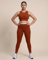 Full-length front view of a model in the Brown Full Coverage Sports Bra and High-Rise Leggings, hands on her hips.