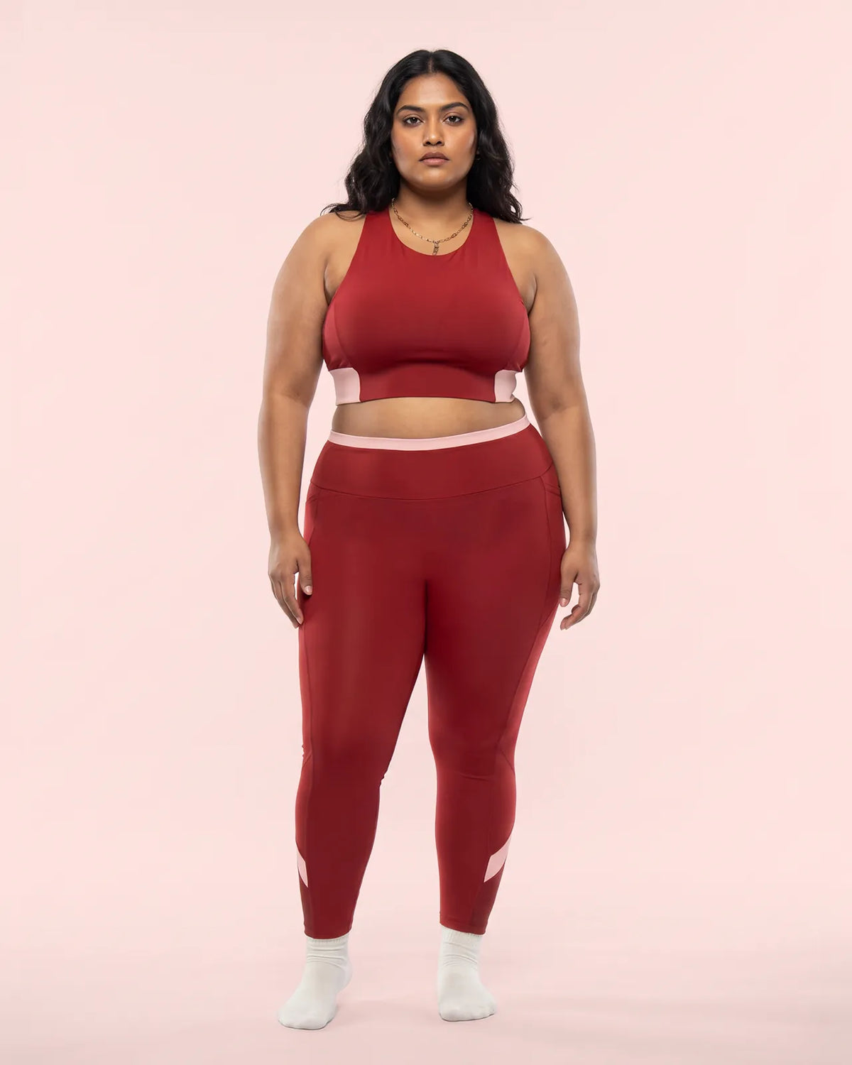 Full-length front view of a model in the Maroon Full Coverage Sports Bra and High-Rise Leggings with a blush pink waistband and calf panels.