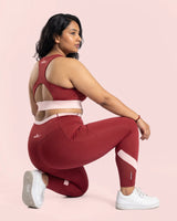 Woman kneeling on one knee, looking over her shoulder, showing the racerback of the Maroon sports bra and the leggings' fit through a deep bend.