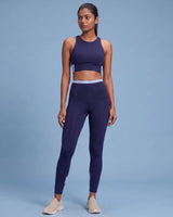 Full-length front view of a model in the Navy Full Coverage Sports Bra and High-Rise Leggings with a light blue waistband and calf panels.