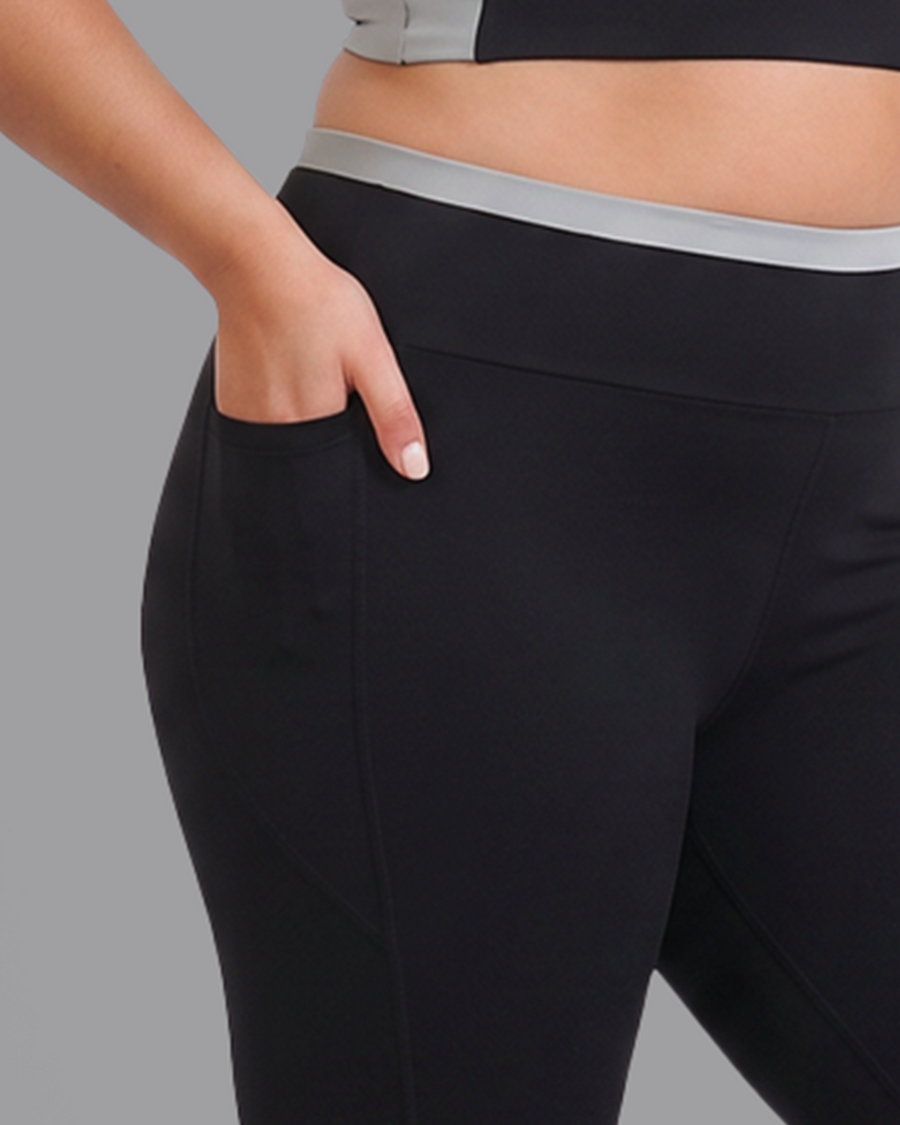 Hand tucked into the deep side pocket of black leggings, below the grey waistband.
