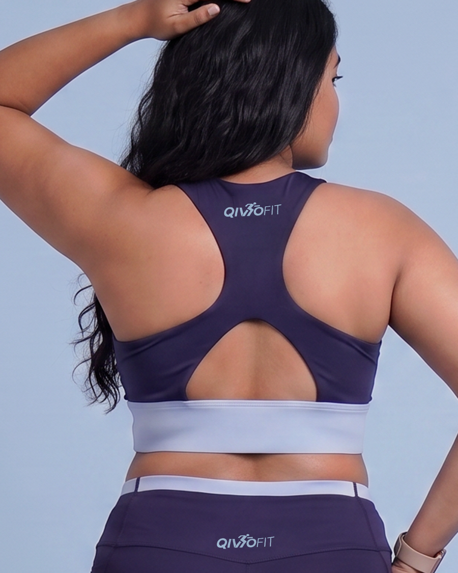 Back view of a woman in the navy sports bra, showing the racerback, keyhole opening and light blue underband.